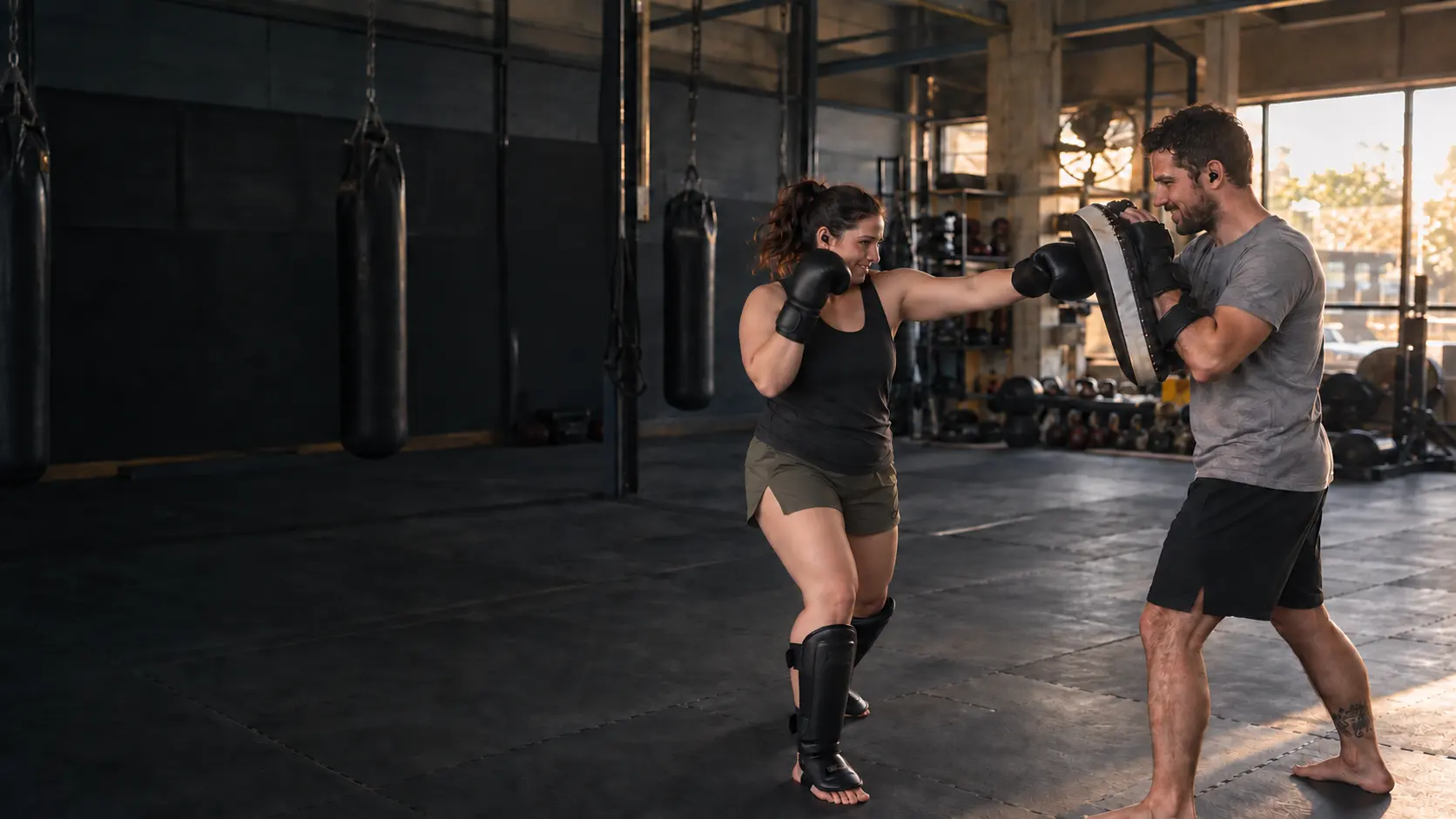 Two friends training together with pads, gloves, shin pads and shared earbuds